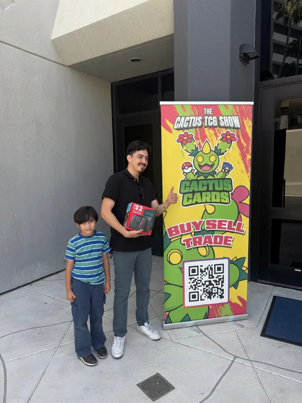 Past grand-prize winner and his son beside the Cactus TCG Show banner at the Mesa, Arizona card show