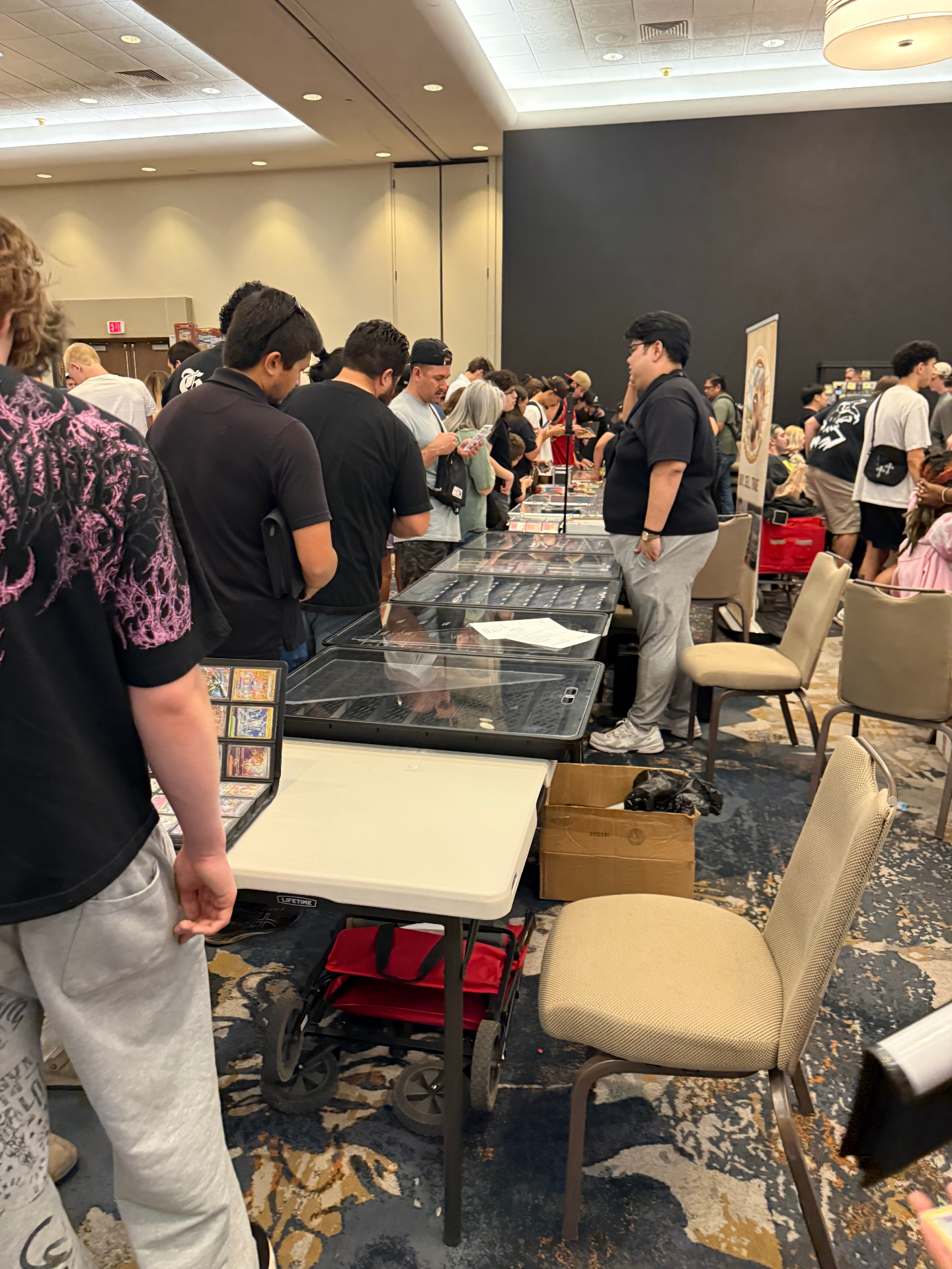 Long row of dealer tables and attendees inside The Cactus card show